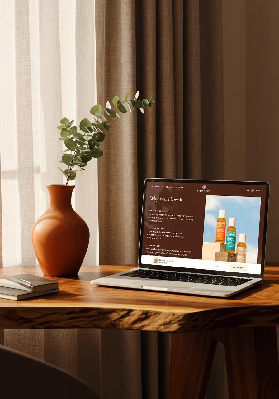 A laptop displaying the Elija's Nature website on a wooden desk, placed next to a terracotta vase with a plant.
