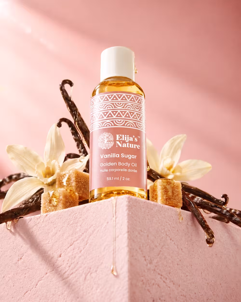 Elija’s Nature Vanilla Sugar Golden Body Oil campaign image with vanilla flowers, pods and golden sugar cubes on a sculptural pink set.