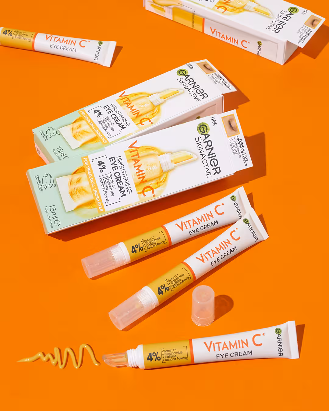 Flat lay of Garnier Vitamin C products including eye cream, serum, and roller displayed with bright orange background.