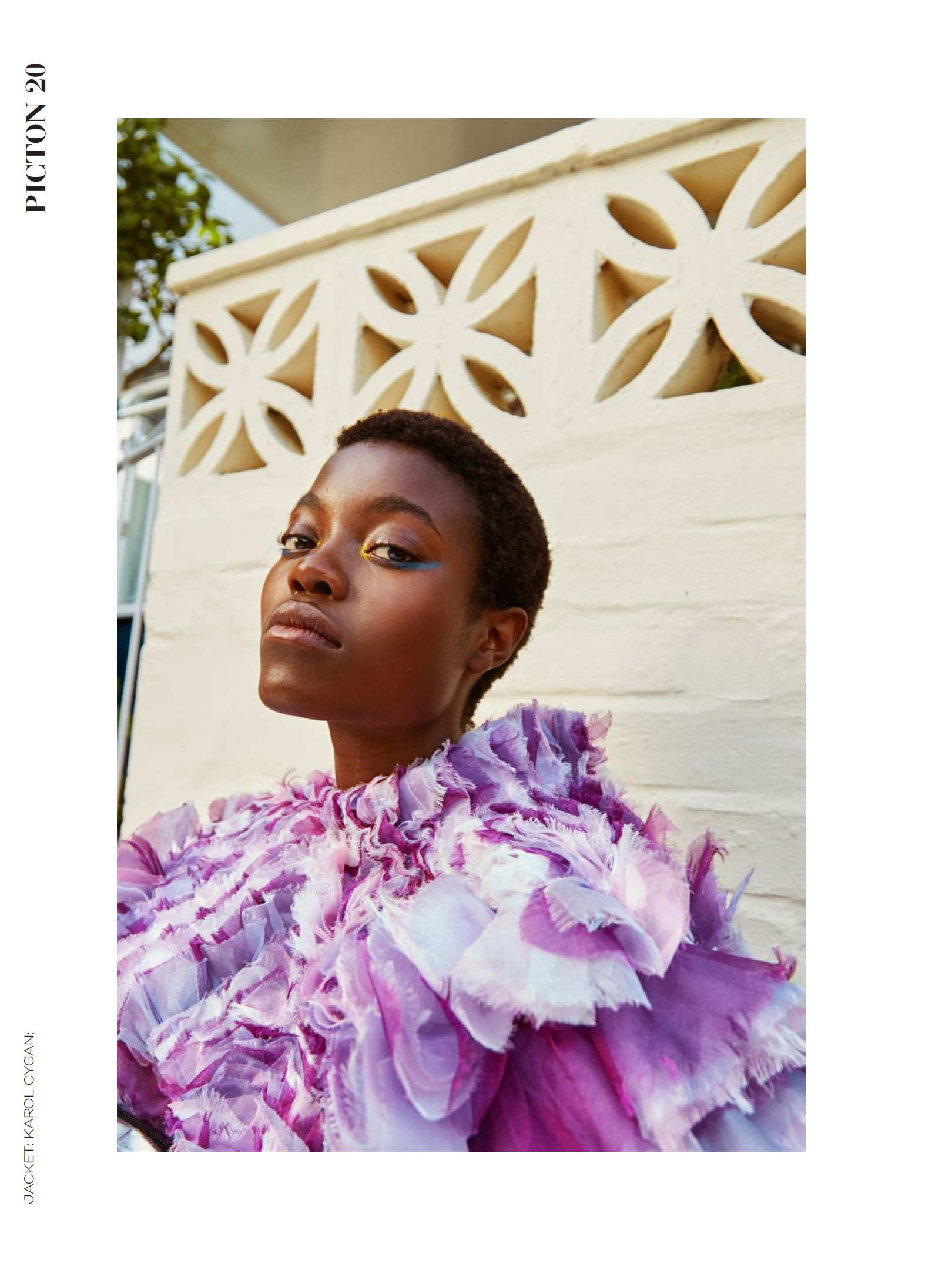 Portrait of Abigail Whitney in a lilac ruffled outfit, leaning against a white patterned wall, Picton Magazine Heatwave editorial.