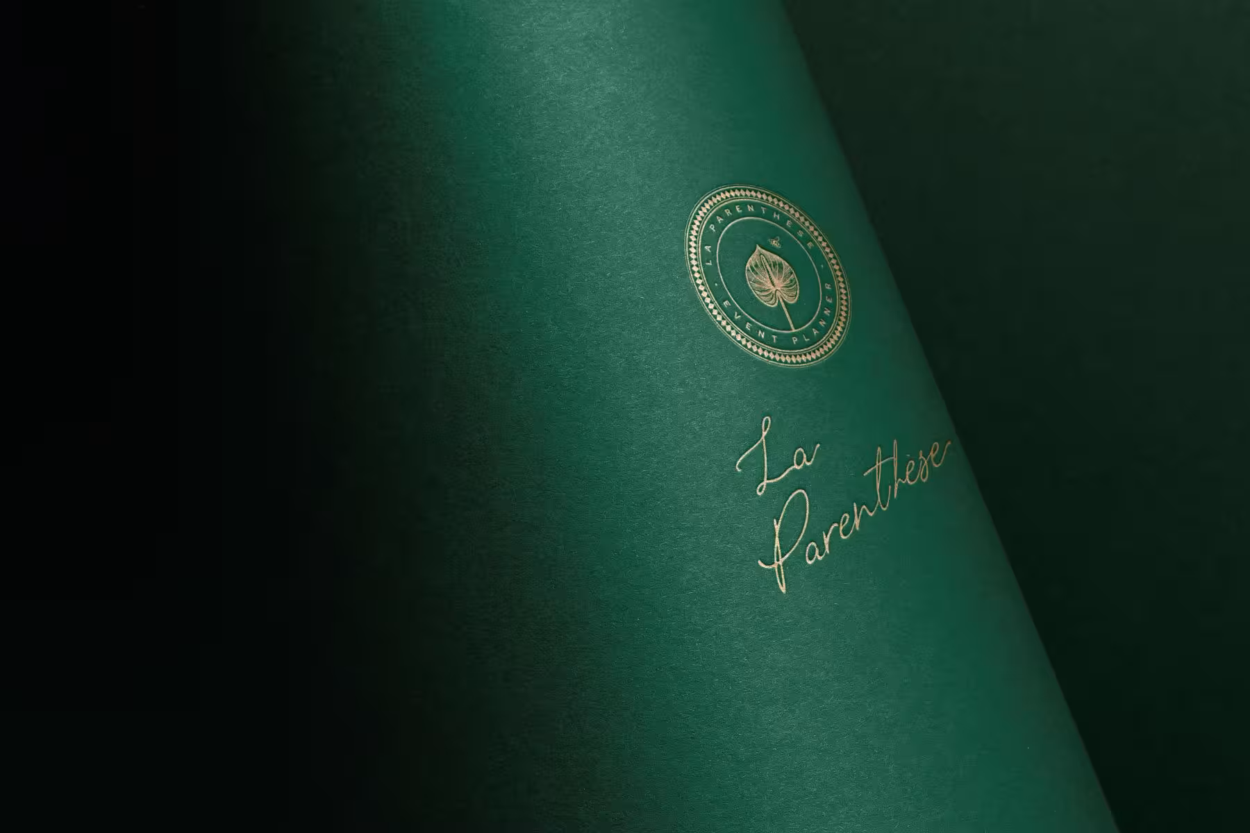 Close-up of La Parenthèse logo embossed in gold on dark green textured paper.