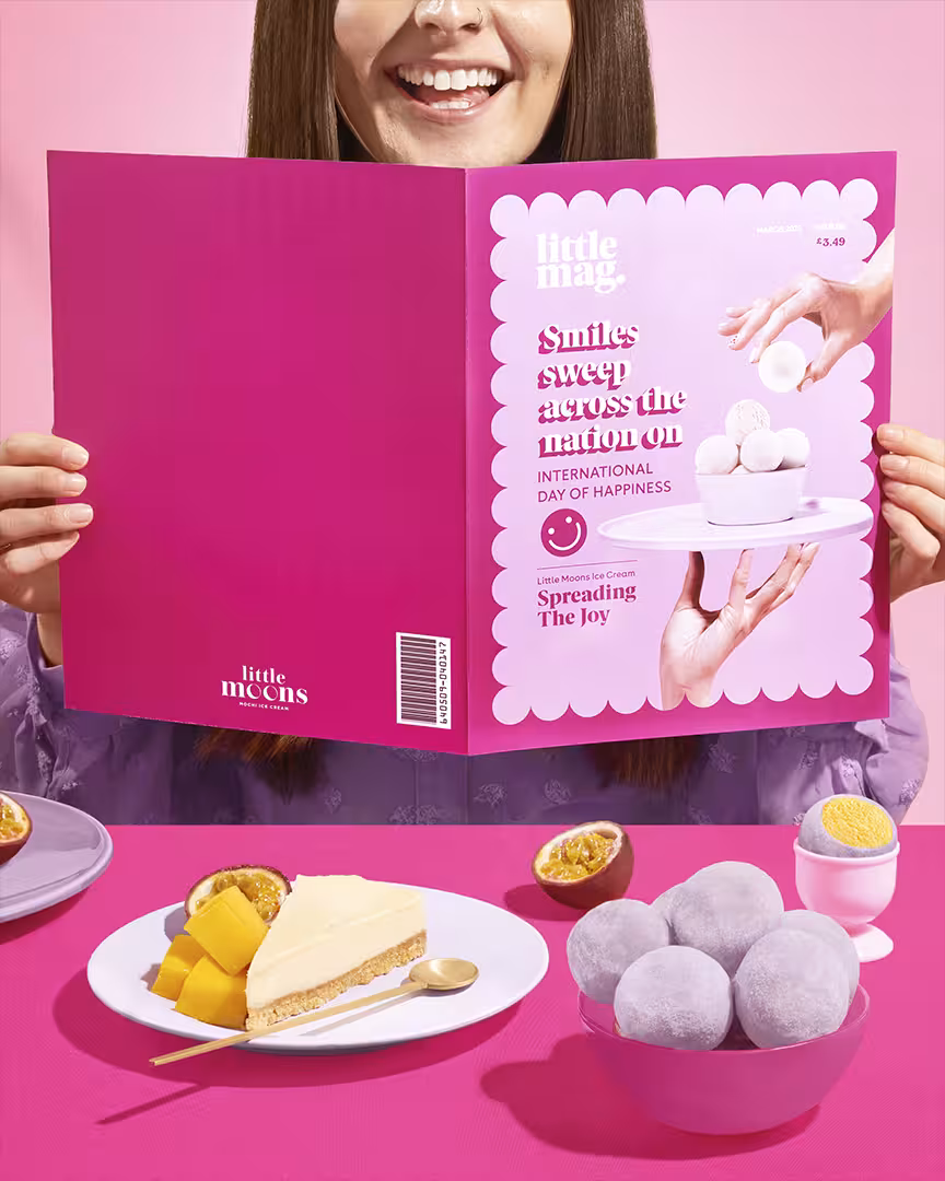 Smiling model holding bright pink magazine styled as Little Moons campaign piece for International Day of Happiness.
