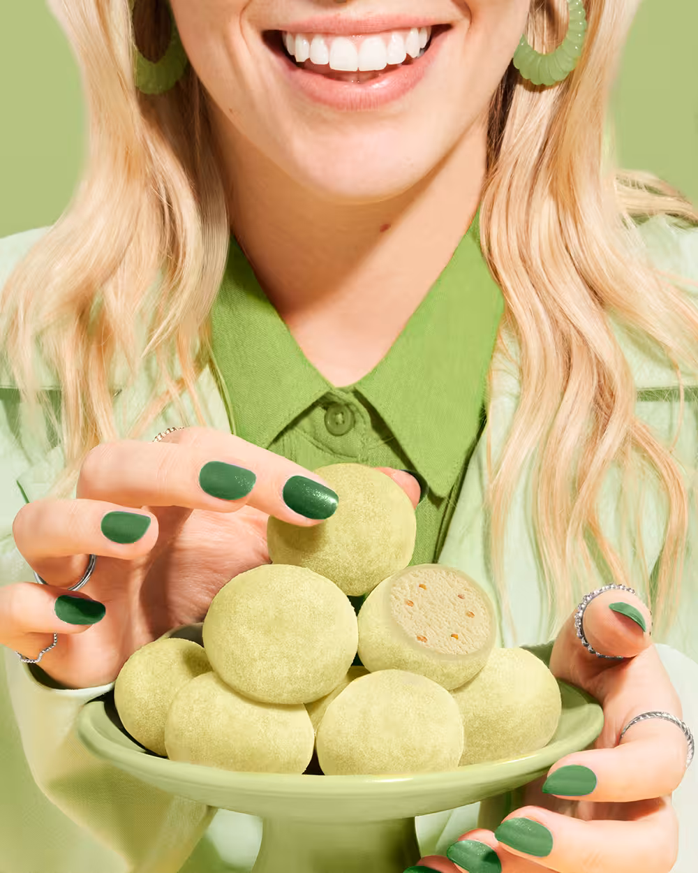 Smiling model in green outfit holding a bowl of pistachio-flavoured Little Moons mochis.