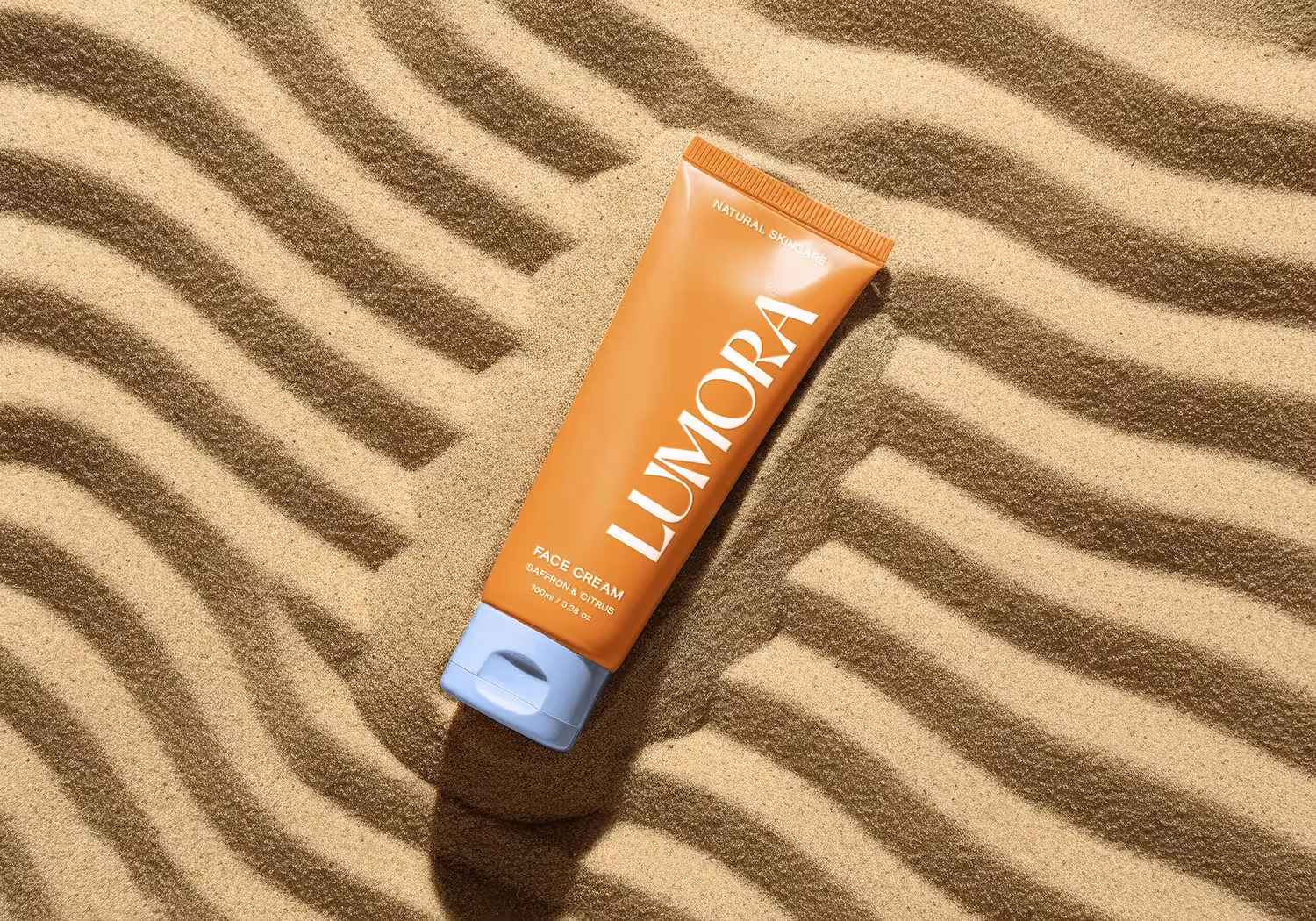 Lumora face cream tube photographed on patterned sand background for product campaign.