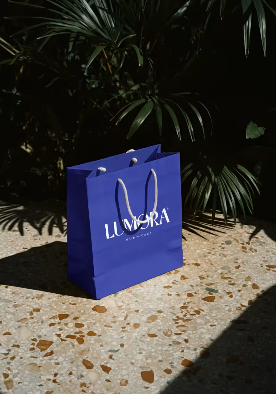 Lumora branded deep blue shopping bag photographed outdoors with natural light and palm leaves.