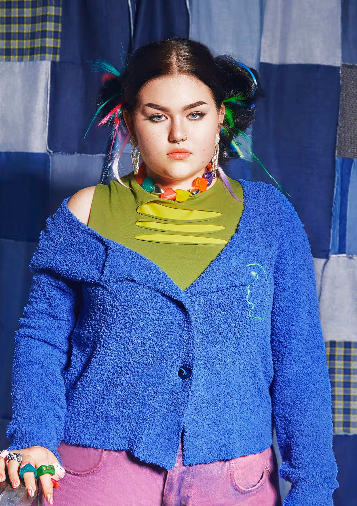 A close-up portrait of Mae Stephens against a blue backdrop, wearing a blue jacket and a green top.