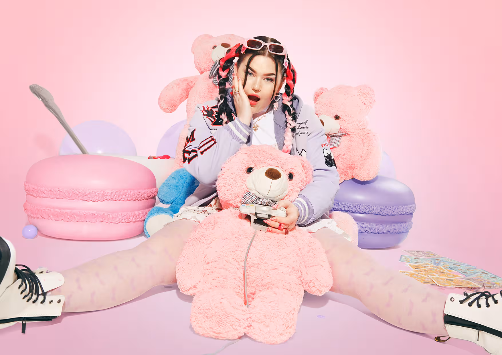 Mae Stephens sitting on the floor, surrounded by several large, fluffy pink teddy bears.