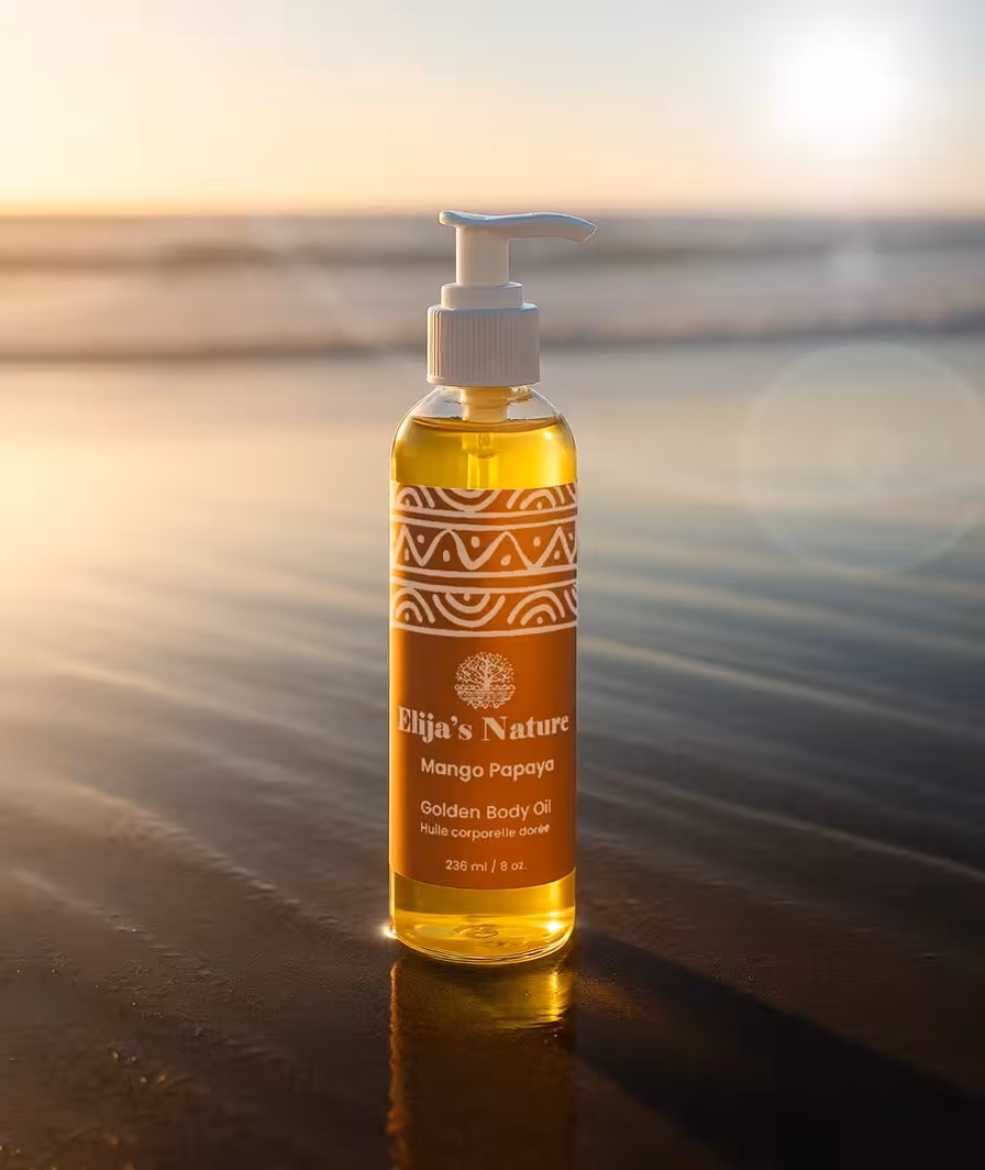 Bottle of Elija’s Nature Mango Papaya Golden Body Oil 8oz standing upright on wet sand at the beach during golden hour.