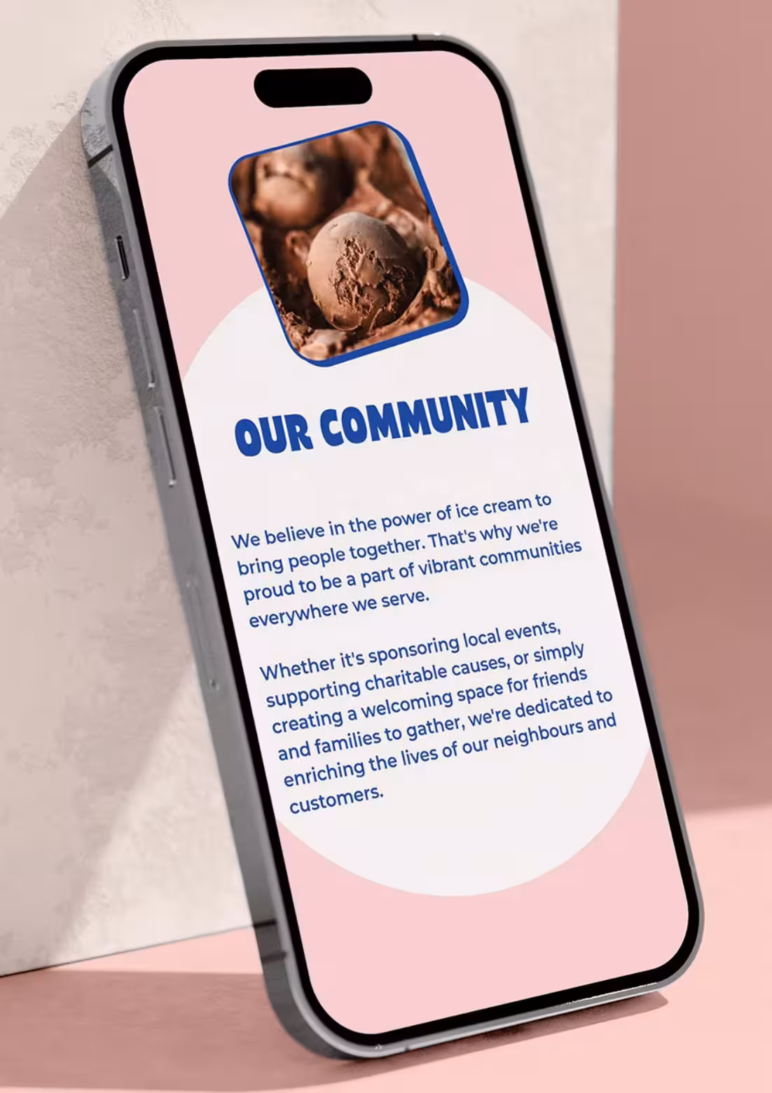 Smartphone displaying “Our Community” section of the Scoops website on a pink surface.