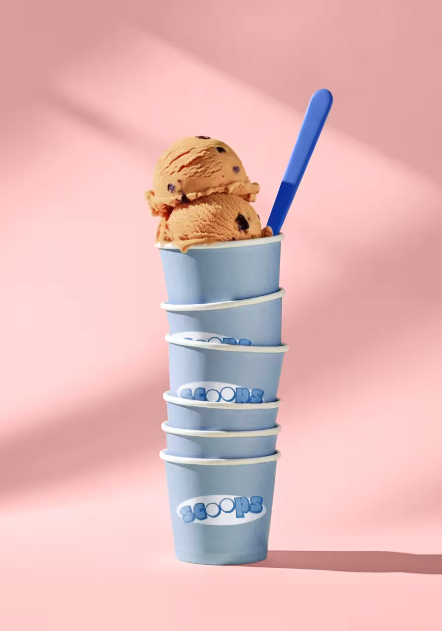 A creative, gravity-defying stack of light blue paper ice cream tubs, balancing two scoops of caramel ice cream on top.