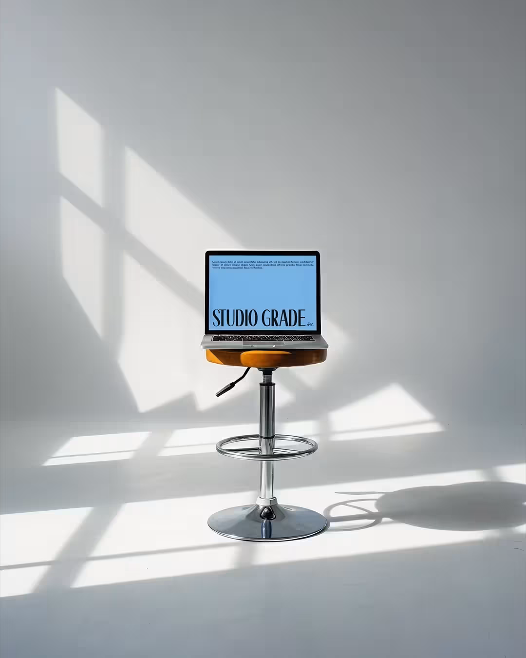 An image of a laptop on a stool in a sunlit studio, with the Studio Grade logo.