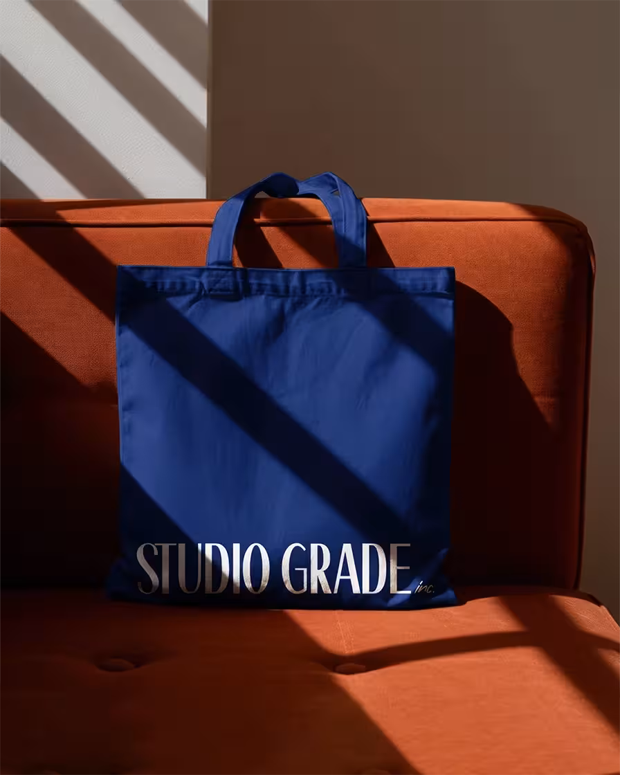 A branded Studio Grade tote bag with the new logo on an orange sofa.